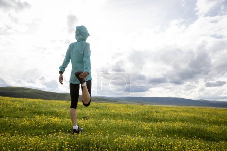 Téléchargez les photos : Femme coureur de sentier étirant les jambes en fleurs à haute altitude prairie montagne - en image libre de droit