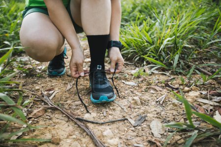 Photo for Woman trail runner tying shoelace on forest trail - Royalty Free Image
