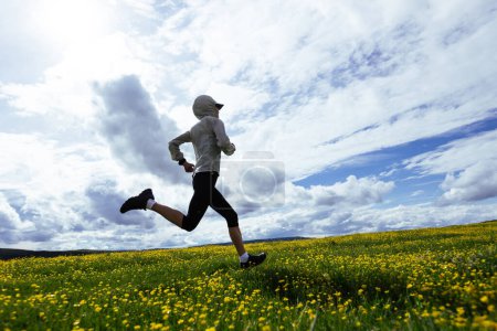 Foto de Mujer trail runner cross country running at high altitude flowering mountain - Imagen libre de derechos
