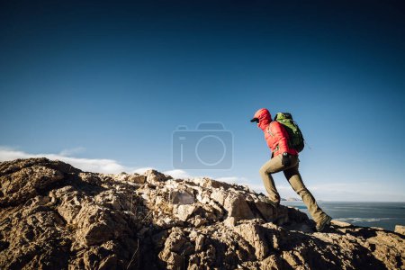 Photo for Woman hiker climbing to mountain top cliff edge at lakeside - Royalty Free Image