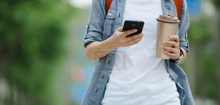 Téléchargez les photos : Les gens utilisent téléphone mobile marche avec tasse de café à la main - en image libre de droit
