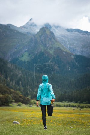 Photo for Woman trail runner stretching legs in flowers at high altitude grassland mountain - Royalty Free Image