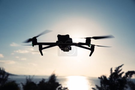 Téléchargez les photos : Silhouette de drone volant qui prend des photos au-dessus de la mer lever du soleil - en image libre de droit