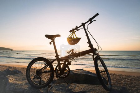 Foto de Una bicicleta plegable en las rocas del amanecer junto al mar - Imagen libre de derechos