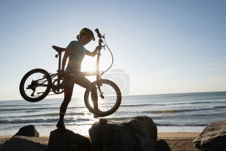 Foto de Mujer tomando una bicicleta plegable en la salida del sol camino costero - Imagen libre de derechos