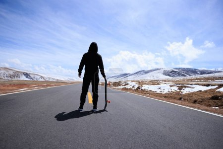 Photo for Skateboarder skateboarding on snowy country road - Royalty Free Image