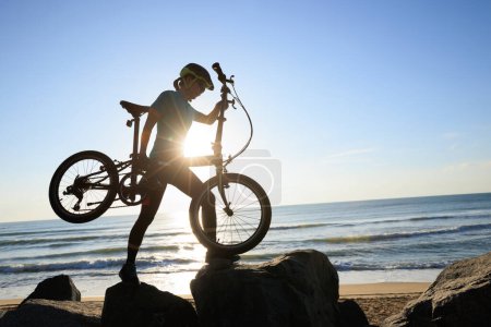 Photo for Woman carrying a folding bike on sunrise seaside road - Royalty Free Image