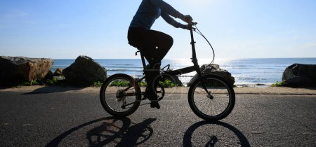 Téléchargez les photos : Vélo pliant équitation sur la route de bord de mer lever du soleil - en image libre de droit
