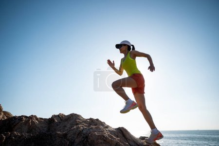 Foto de Corredor mujer corriendo al amanecer en las montañas rocosas junto al mar - Imagen libre de derechos