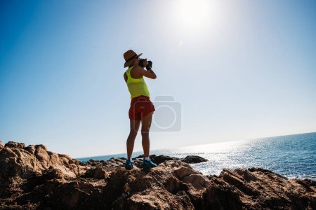 Téléchargez les photos : Femme prenant des photos sur le lever du soleil bord de mer montagnes rocheuses - en image libre de droit