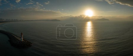 Téléchargez les photos : Phare rayé rouge et blanc haut sur le bord de la mer au soleil du matin. Ciel bleu avec des nuages blancs. Vacances d'été, vacances en mer concept - en image libre de droit