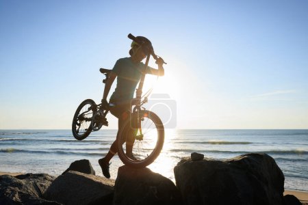 Téléchargez les photos : Femme portant un vélo pliant au lever du soleil bord de mer - en image libre de droit