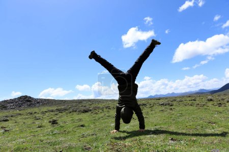 Téléchargez les photos : Femme randonneur faisant un handstand sur prairie de montagne de haute altitude - en image libre de droit