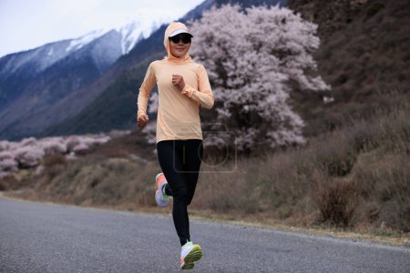 Photo for Woman running in spring tibet,peach flowers blooming and snow capped mountains in the background, China - Royalty Free Image