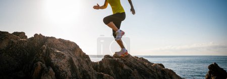Foto de Mujer corredor piernas corriendo en la salida del sol mar rocas - Imagen libre de derechos