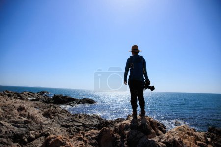 Téléchargez les photos : Femme photographe profiter de la vue sur les rochers de bord de mer lever du soleil - en image libre de droit