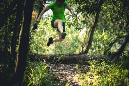 Photo for Woman trail runner jumping over a fallen tree trunk in tropical forest - Royalty Free Image