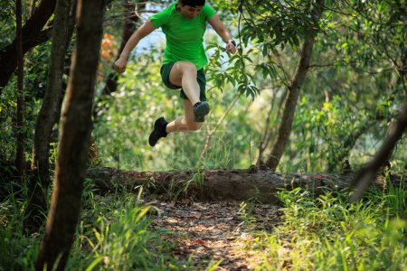 Téléchargez les photos : Femme coureuse de sentier sautant par-dessus un tronc d'arbre tombé dans la forêt tropicale - en image libre de droit