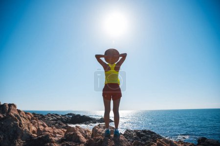 Foto de Mujer disfrutar de la vista en la salida del sol rocas junto al mar - Imagen libre de derechos