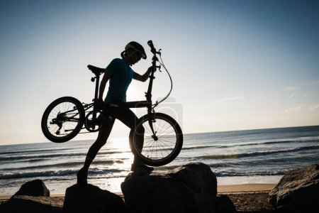 Foto de Mujer tomando una bicicleta plegable al amanecer junto al mar - Imagen libre de derechos