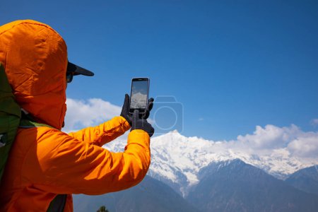Téléchargez les photos : Sac à dos femme prenant des photos de montagnes de haute altitude avec téléphone intelligent - en image libre de droit