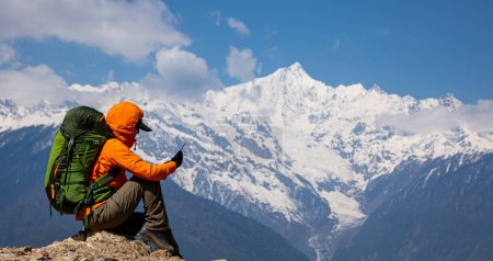 Téléchargez les photos : Sac à dos femme prenant des photos de montagnes de haute altitude avec téléphone intelligent - en image libre de droit