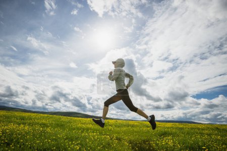 Foto de Mujer trail runner cross country running in high altitude flowering mountains - Imagen libre de derechos