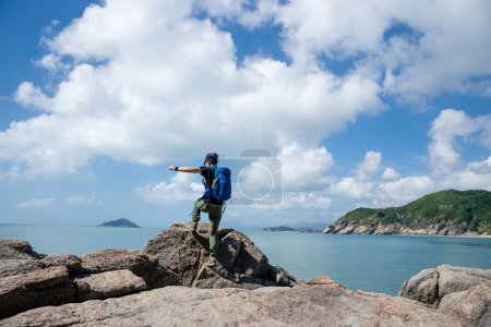 Foto de Senderista saltando sobre roca junto al mar - Imagen libre de derechos
