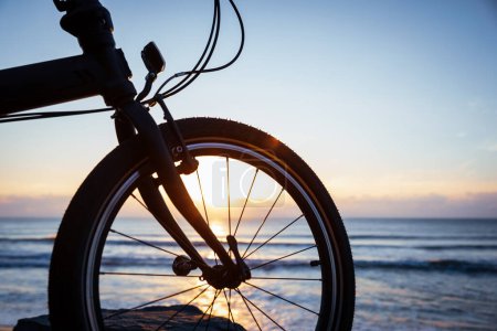Téléchargez les photos : Un vélo pliant sur la roche de bord de mer lever du soleil - en image libre de droit