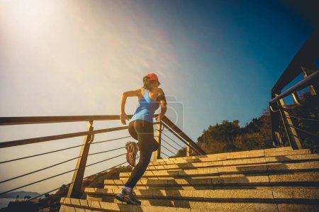 Téléchargez les photos : Mode de vie sain femme sportive courant sur les escaliers en pierre au lever du soleil bord de mer - en image libre de droit