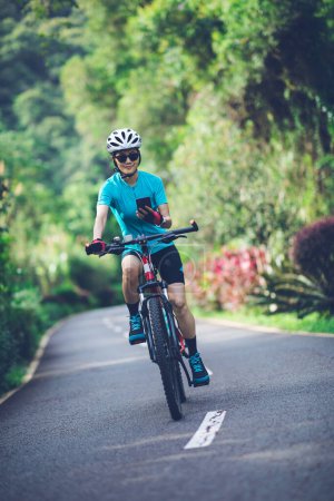 Téléchargez les photos : Femme utilisant le vélo de téléphone intelligent sur le sentier du parc tropical en été - en image libre de droit