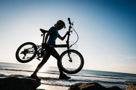 Téléchargez les photos : Femme prenant un vélo pliant au lever du soleil bord de mer - en image libre de droit