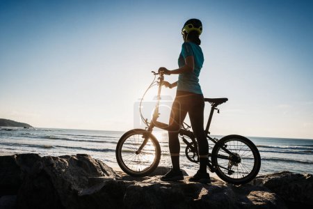 Photo for Woman taking a folding bike on sunrise seaside - Royalty Free Image