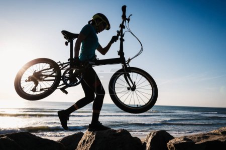 Photo for Woman taking a folding bike on sunrise seaside - Royalty Free Image