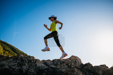 Foto de Corredor mujer corriendo en las rocas del amanecer junto al mar - Imagen libre de derechos