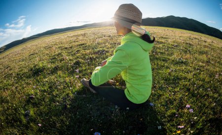 Woman sit on flowers and grass in high altitude mountains