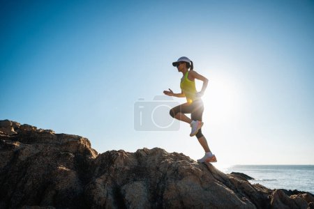 Foto de Corredor mujer corriendo en las rocas del amanecer junto al mar - Imagen libre de derechos