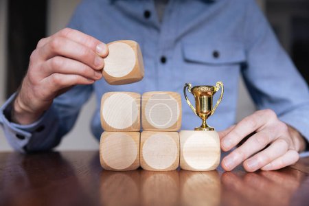 Téléchargez les photos : Homme d'affaires organisant de grands blocs de bois avec un trophée gagnant. Succès des entreprises. - en image libre de droit