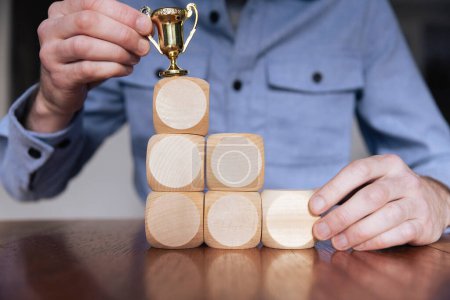 Téléchargez les photos : Homme d'affaires organisant de grands blocs de bois avec un trophée gagnant. Succès des entreprises. - en image libre de droit