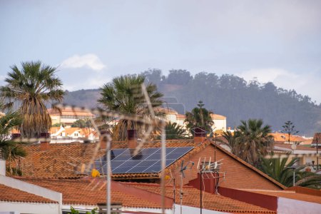 Téléchargez les photos : Panneaux solaires sur le toit d'une maison unifamiliale de briques rouges et de tuiles rouges, avec des palmiers et un paysage d'arbres en arrière-plan. Tenerife, Îles Canaries, Espagne - en image libre de droit