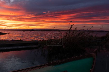 Photo for Beautiful sunset with a sky full of orange and magenta clouds with a boat in the foreground and bushes, surrounded by rice fields and marshes, in the Albufera natural park, in Valencia, Spain, Europe - Royalty Free Image