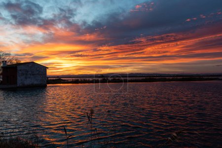 Photo for Beautiful sunset with a sky full of orange and magenta clouds with a farmer's house, surrounded by rice fields and marshes, in the Albufera natural park, in Valencia, Spain, Europe - Royalty Free Image