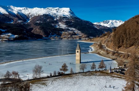 CURON VENOSTA, 6. Januar 2023: Touristen gehen auf dem zugefrorenen Reschensee spazieren. Es ist ein künstlicher Stausee im Westen Südtirols bei Graun im Vinschgau, Italien