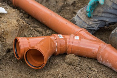 Téléchargez les photos : Travailleur de la construction met des tuyaux d'égout en PVC sur place branches dans le système de tuyaux d'égout - en image libre de droit