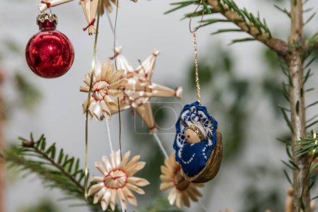 Tree hangings with straw stars, Christmas ball and nativity scene on the Christmas tree - detail