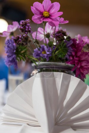 Foto de Servilleta de tela blanca plegada y colorido ramo de flores como decoración de mesa - Imagen libre de derechos