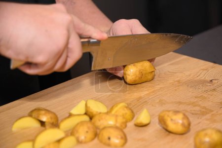 Photo for Chef cuts raw potatoes into wedges with kitchen knife - close-up - Royalty Free Image