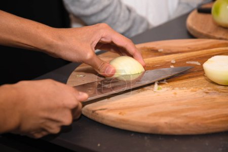 Female chef cuts white onion on wooden plate with vegetable knife