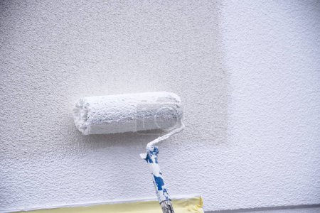 Photo for Painter paints the facade with a paint roller on a construction site - craftsmanship - Royalty Free Image