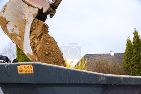 Photo for Bucket of backhoe at construction site dumps earth into dump truck - close-up - Royalty Free Image